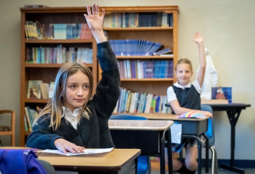 Two schoolgirls raising hands in a classroom.