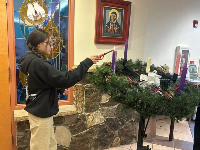 A person lighting a candle on a wreath in a cozy room.