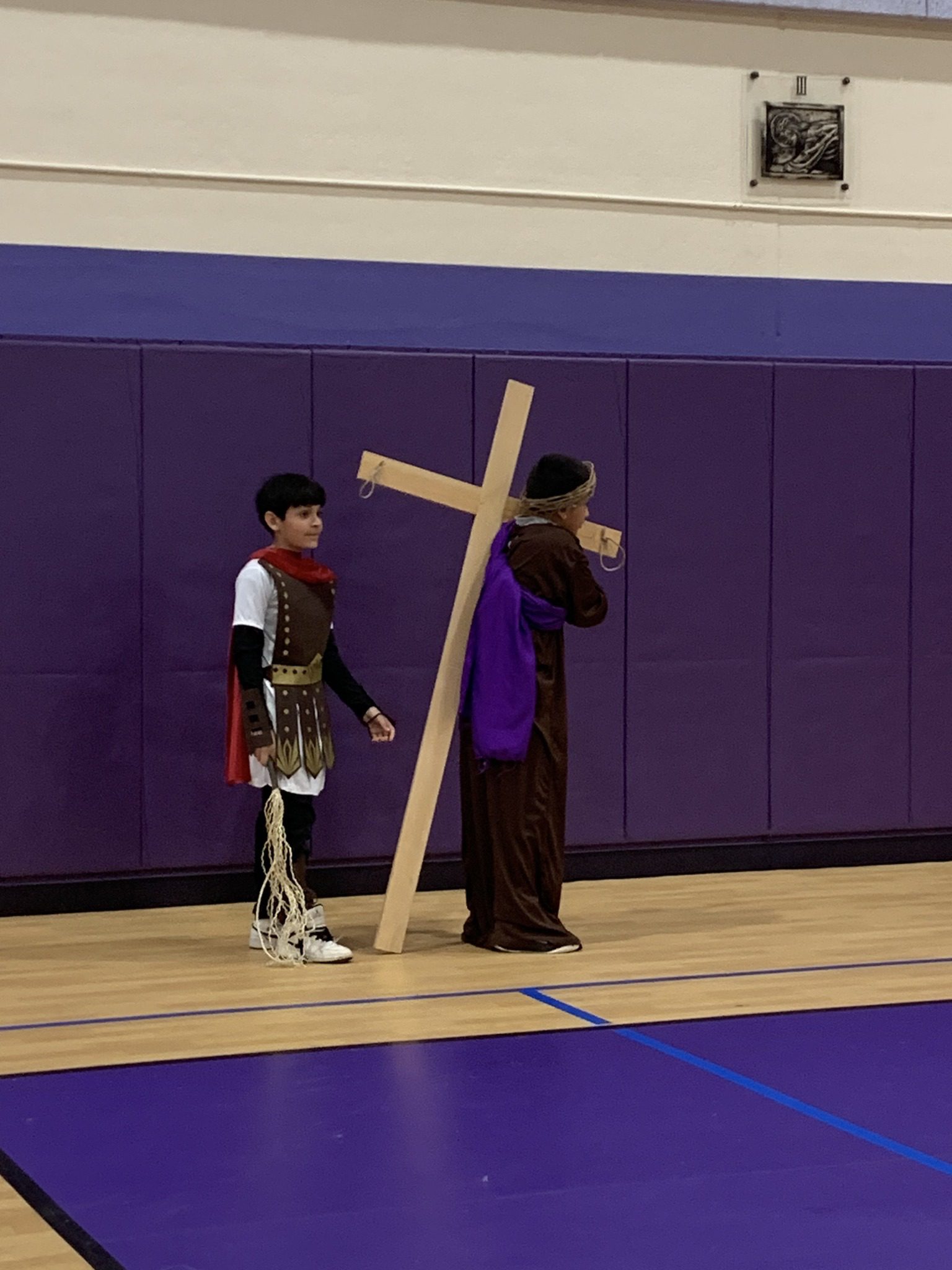 Two boys in a gym, one holding a large wooden cross.