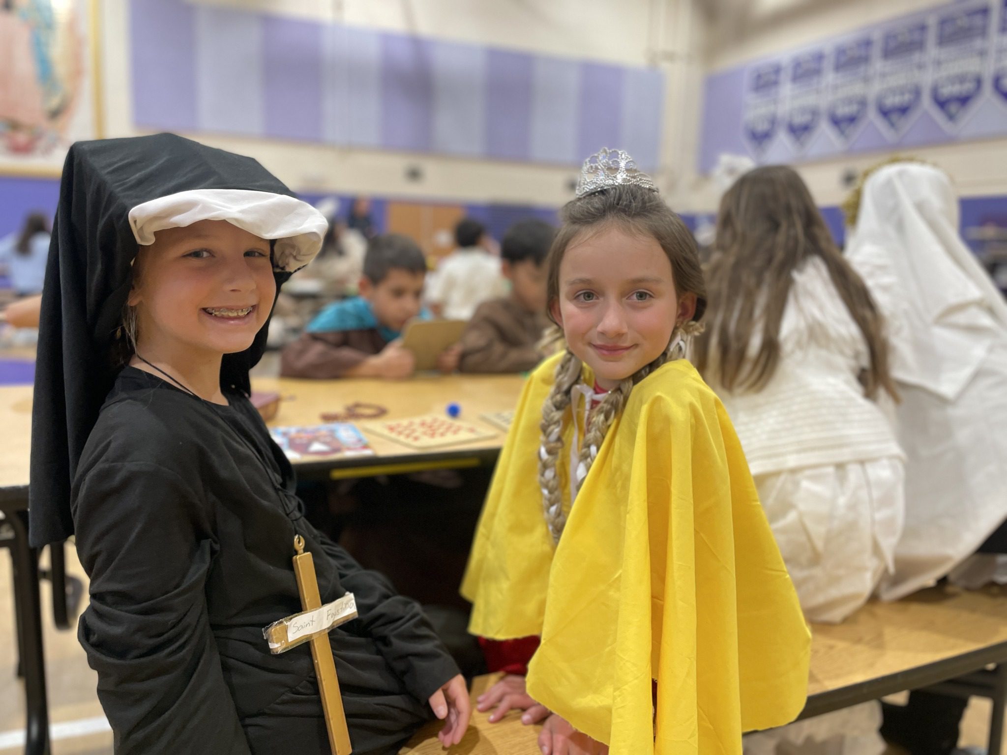 Two children in costume sitting at a table in a busy room.