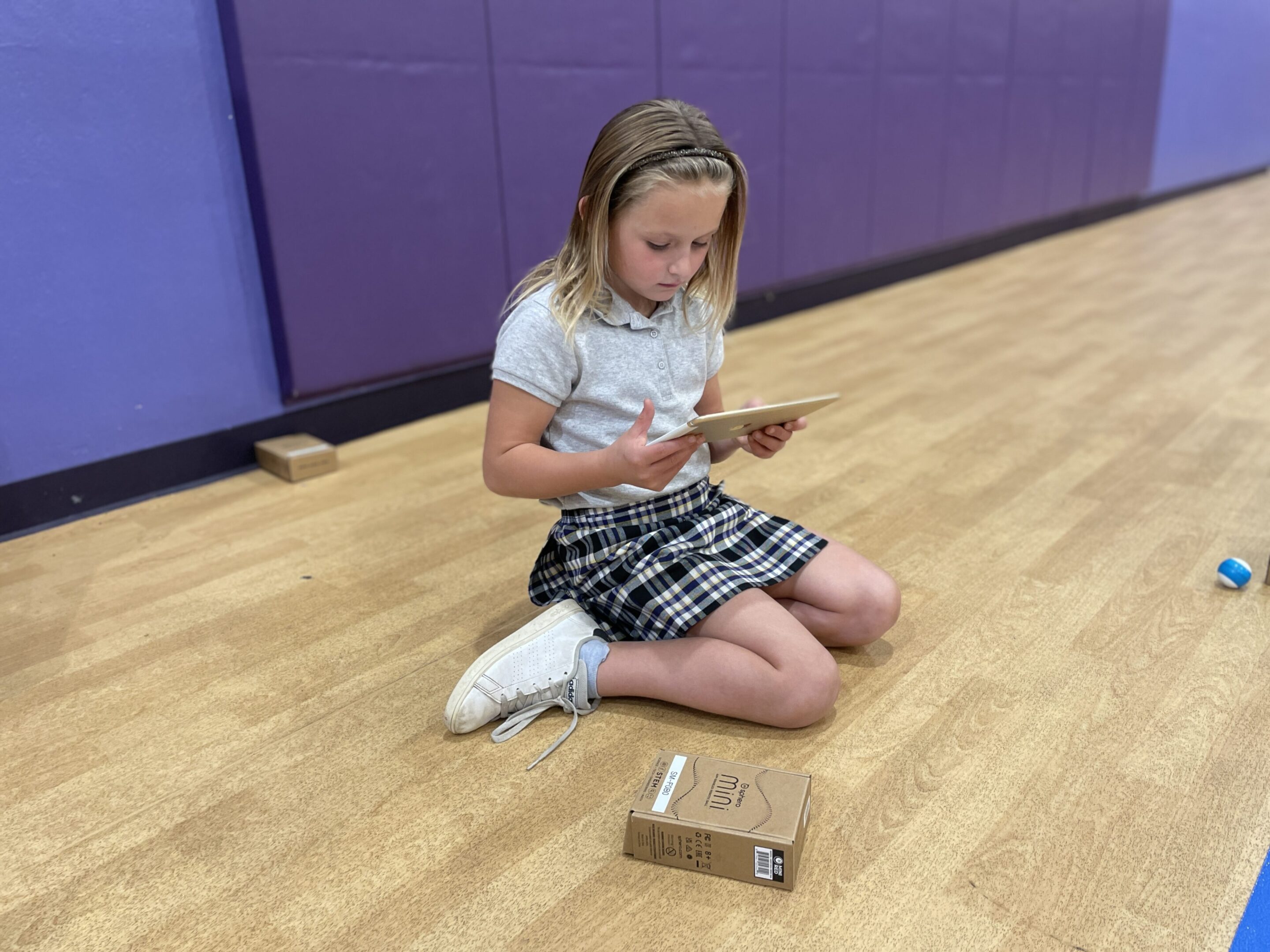 A girl sitting on a gym floor, focused on a phone.