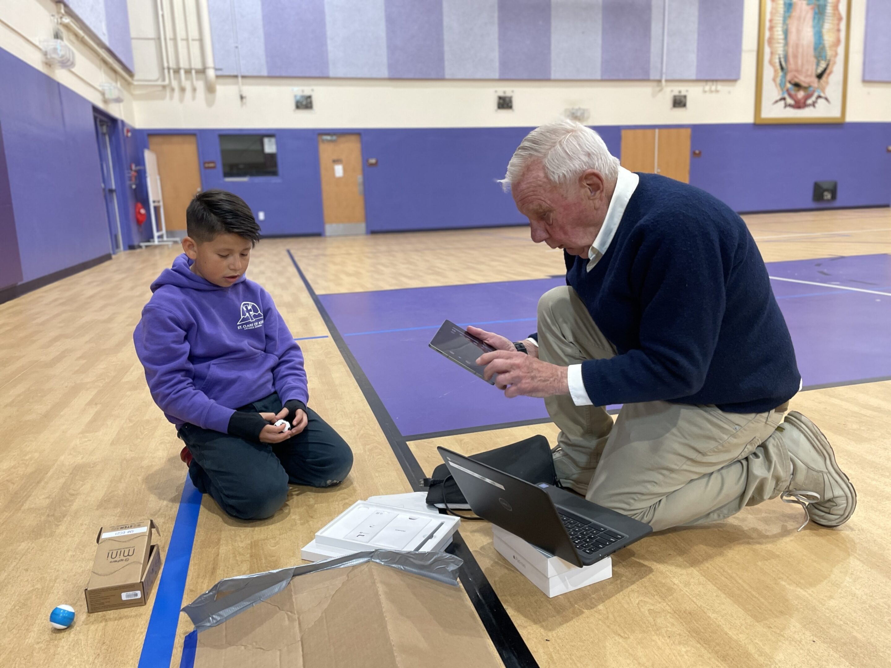 An elderly man and a boy using a tablet in a gymnasium.