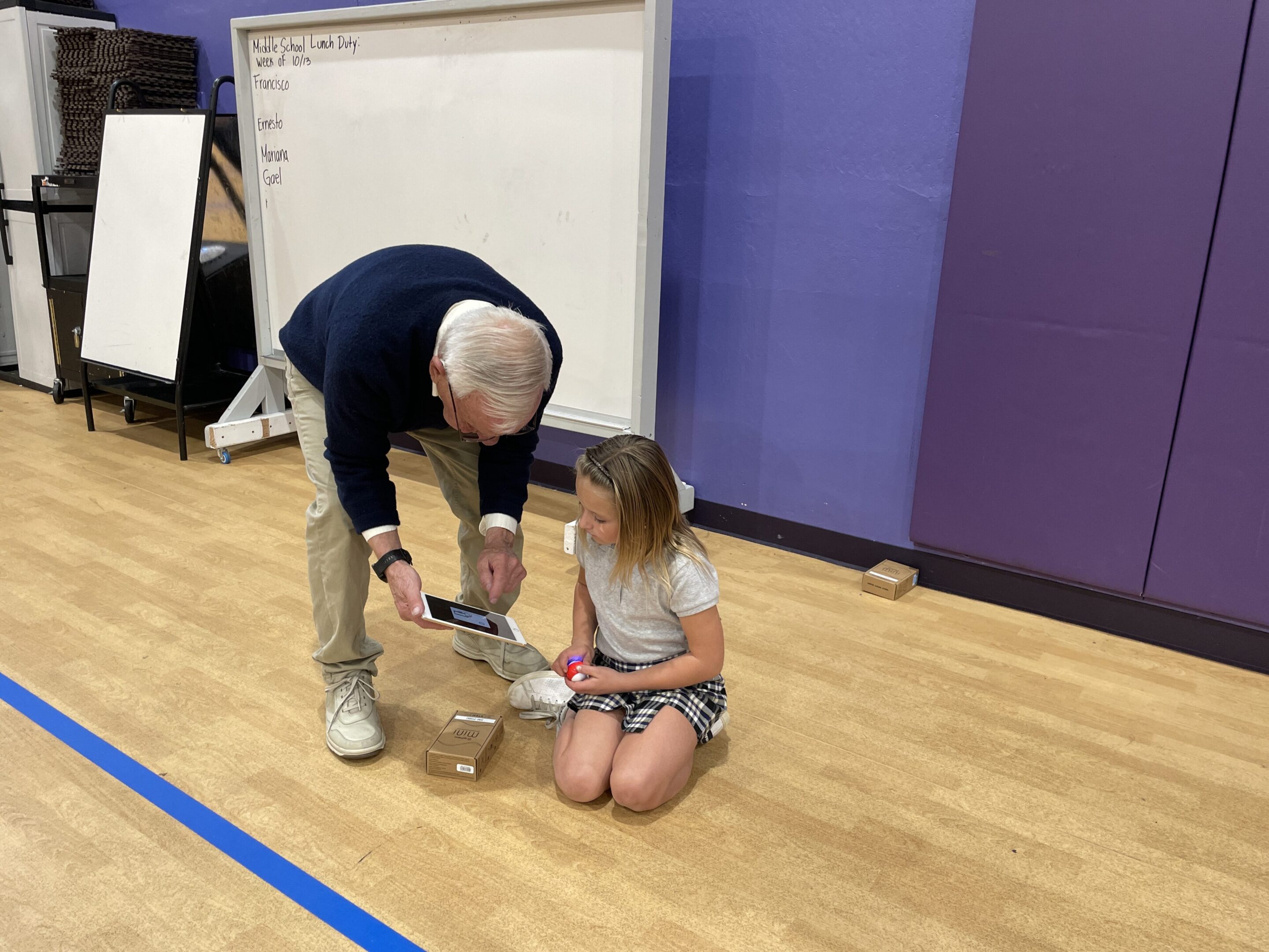 Man helping a girl tie her shoe on a gym floor.