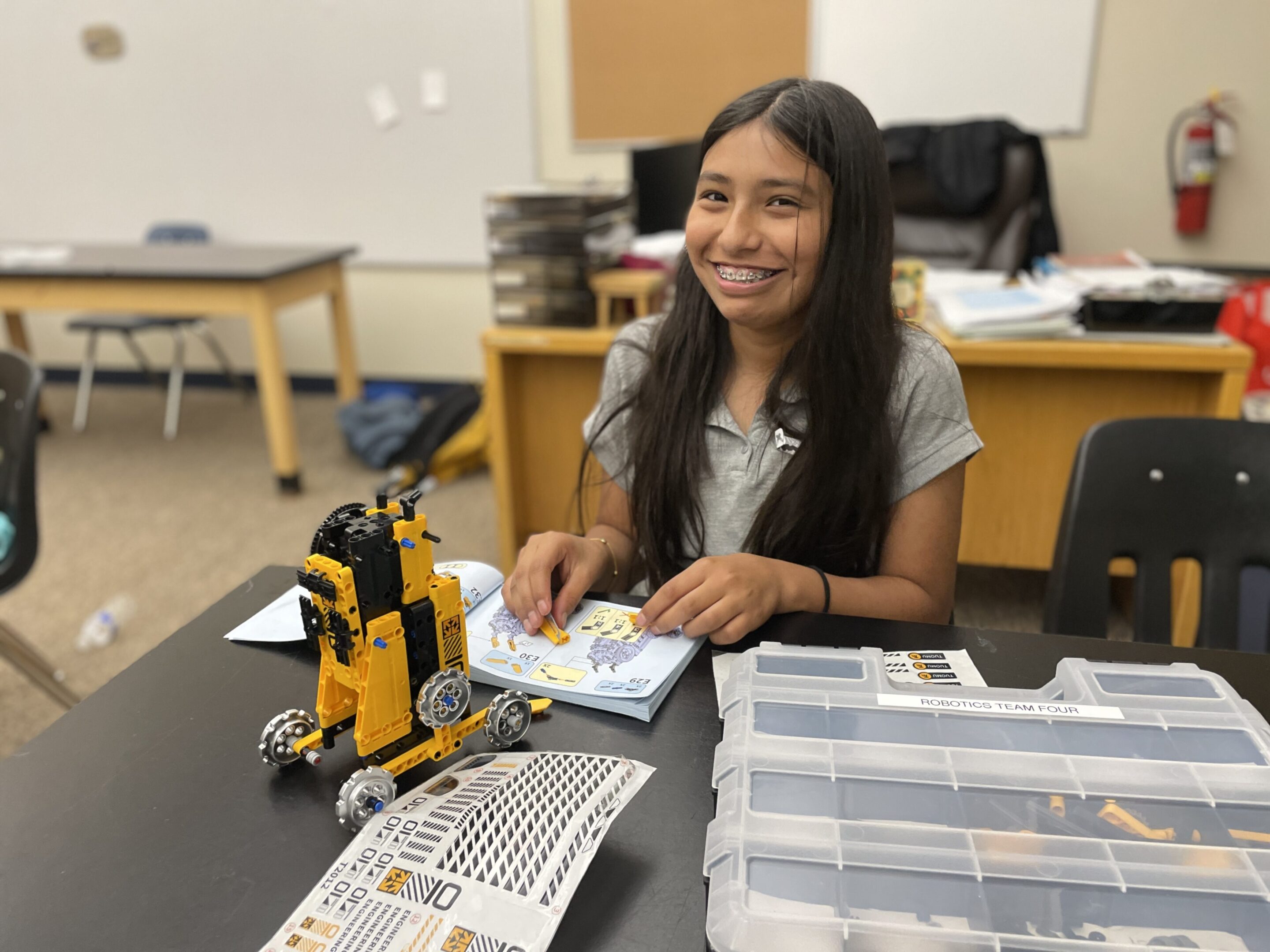 A girl smiling at a table with a robot and electronics kits.