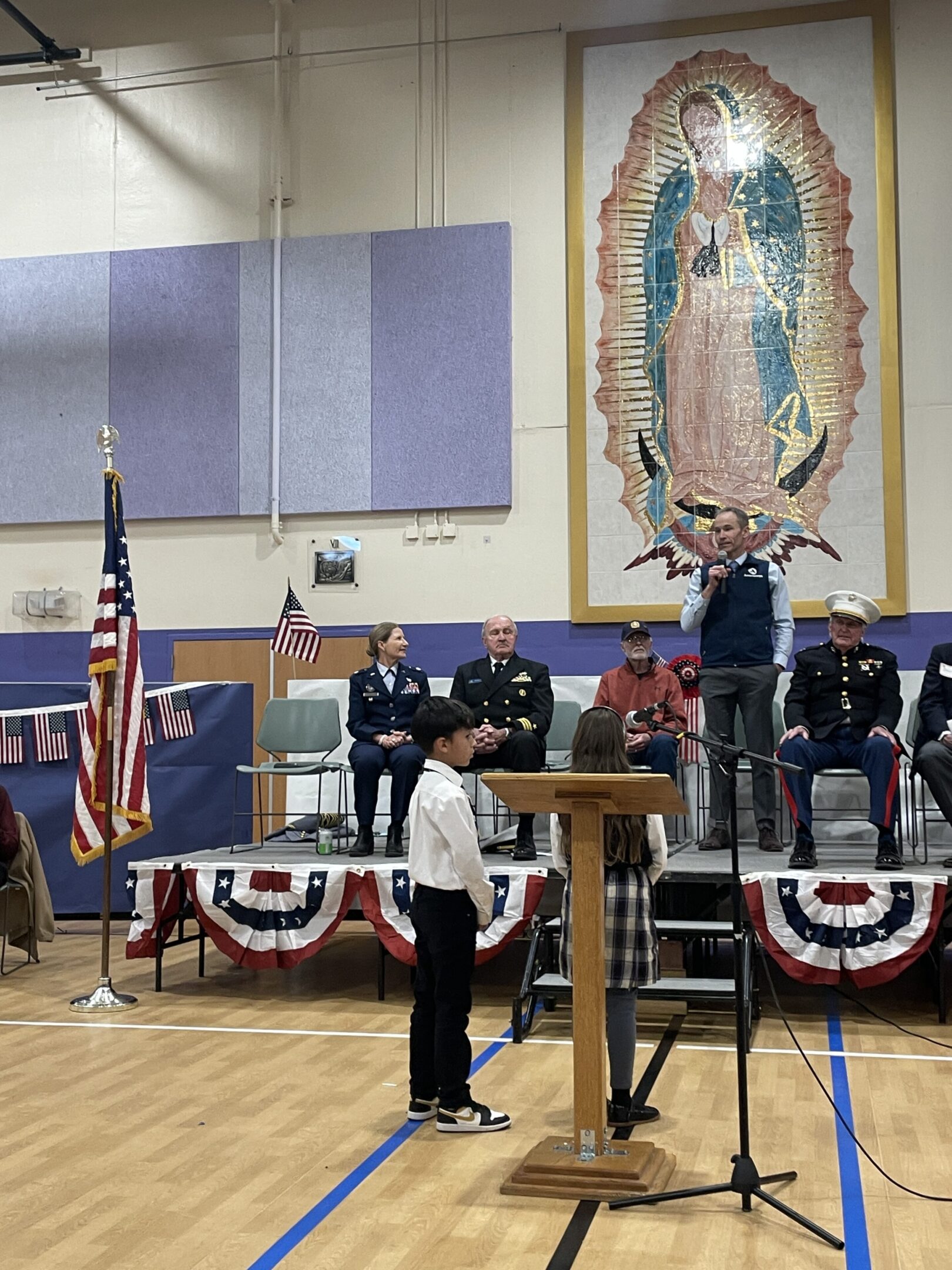 Ceremonial flag presentation during a formal event in a decorated gymnasium.