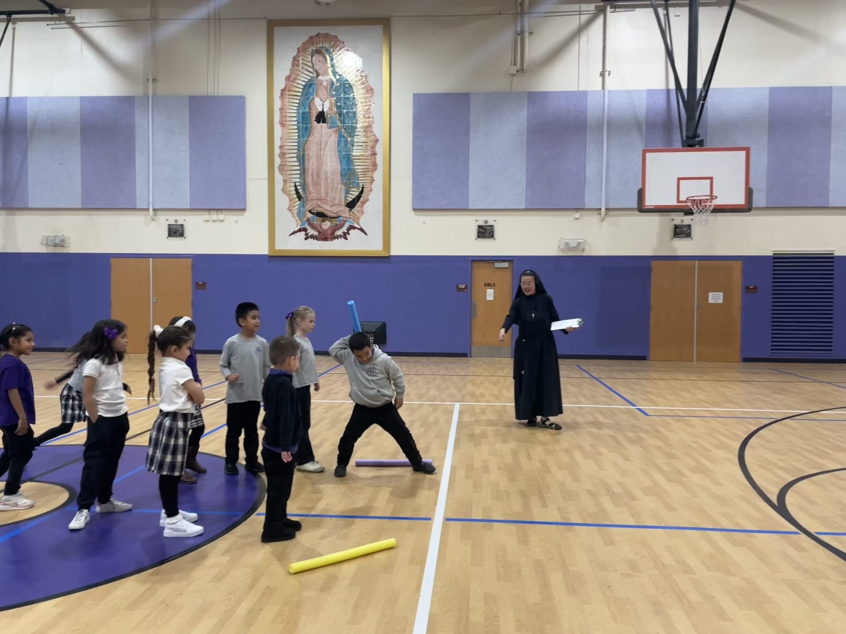 Children playing a game with a nun in a gymnasium.