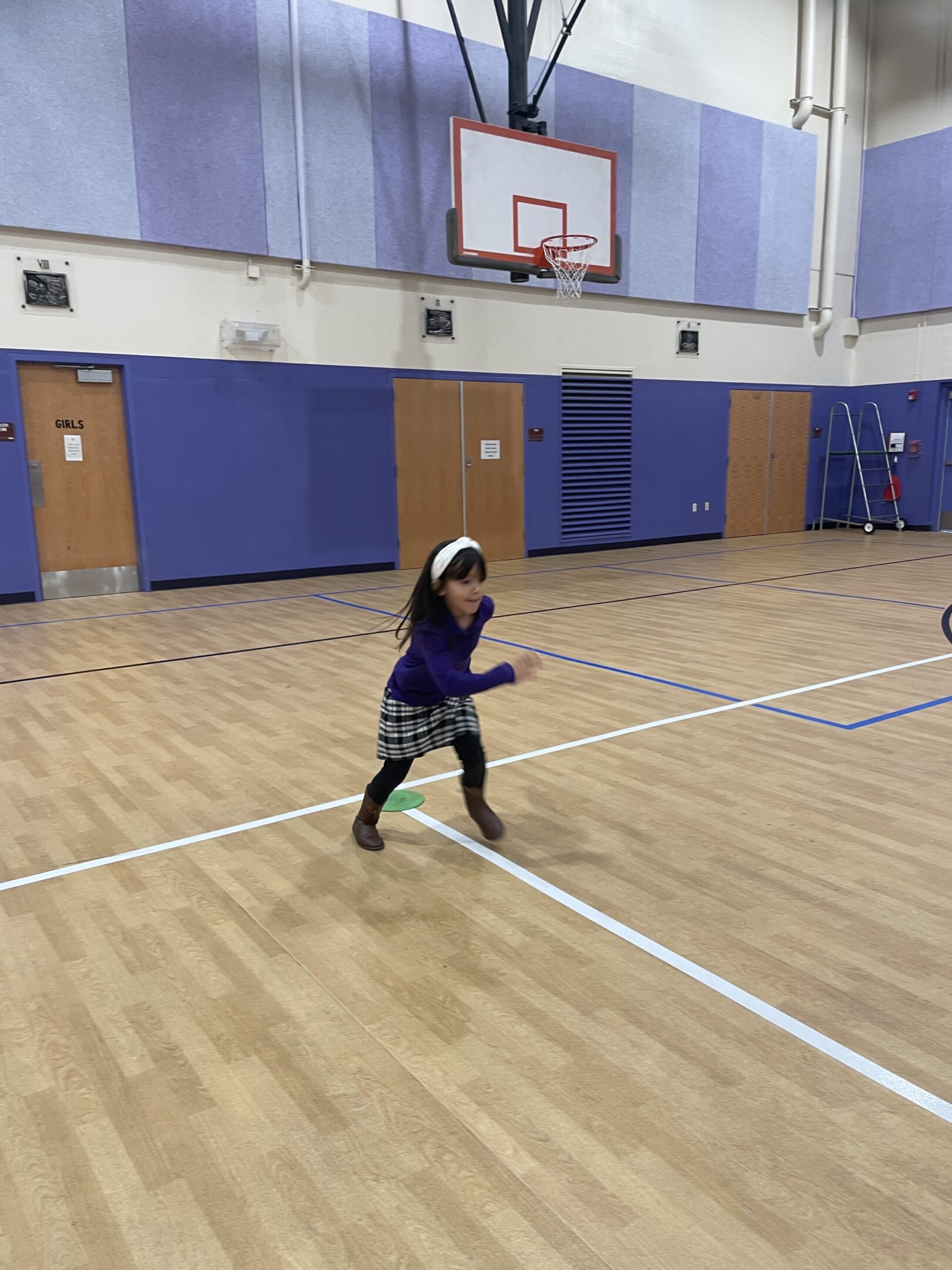 Child playing badminton indoors on a gym court.