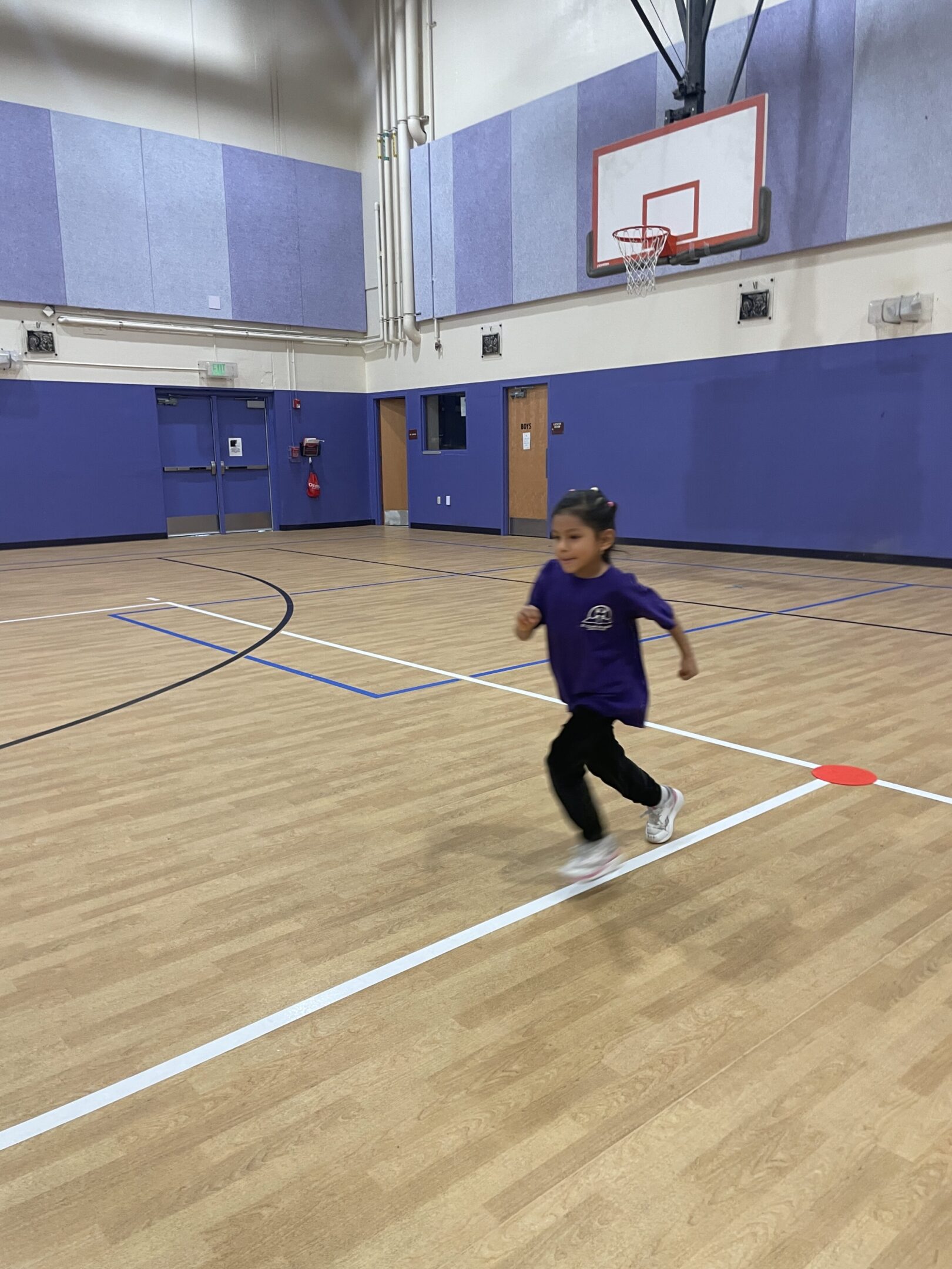 A child runs indoors on a gym court wearing a purple top.