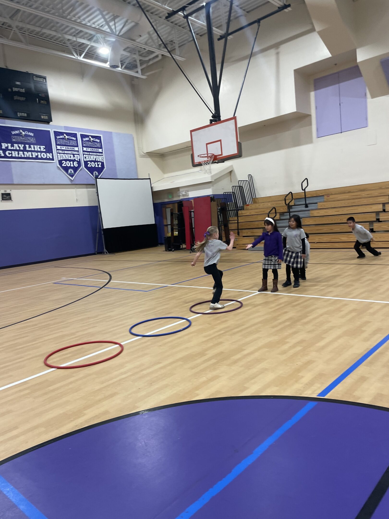 Children playing a basketball game in a gymnasium with hoops and hula hoops.
