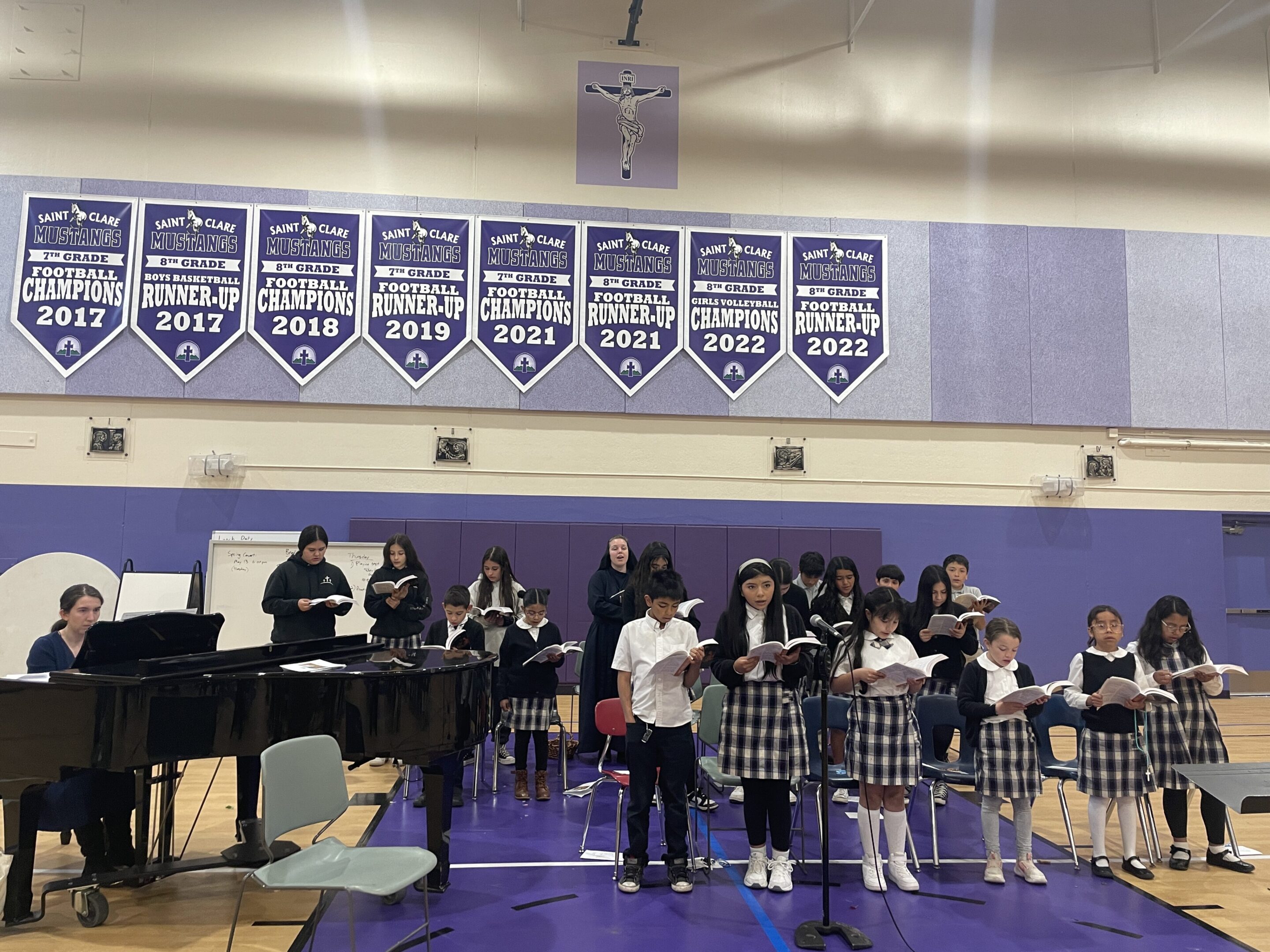 Students perform in a school band inside a gymnasium with championship banners overhead.