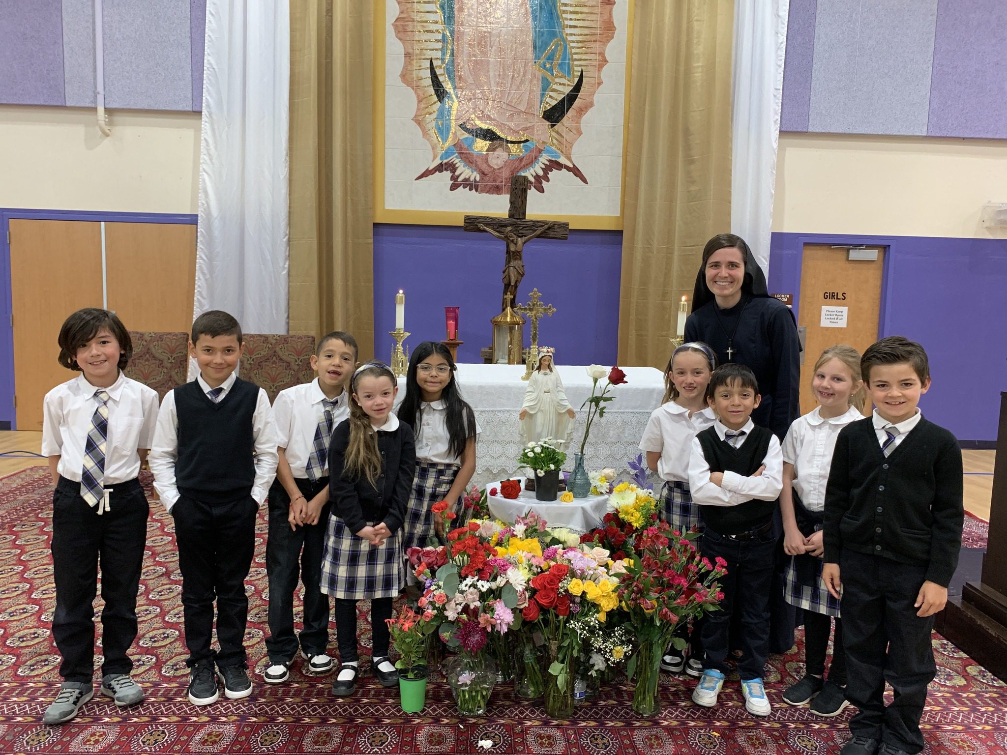 A group of children and an adult posing near a flower-adorned altar.