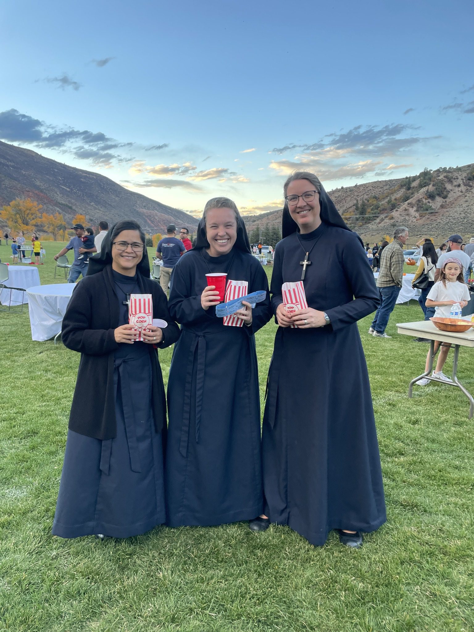 Three nuns holding books outdoors at a daytime event.