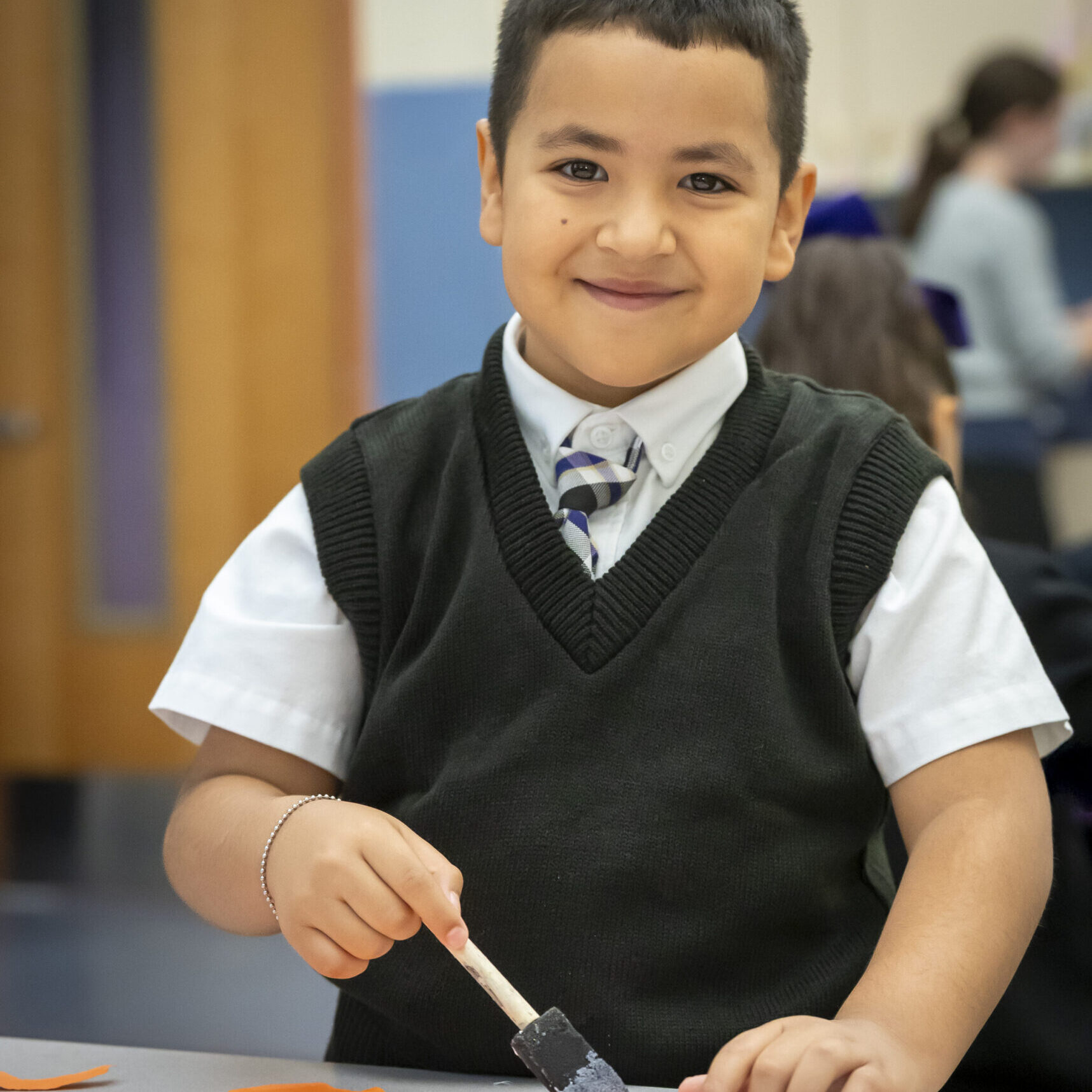Young boy in school uniform smiling while painting.