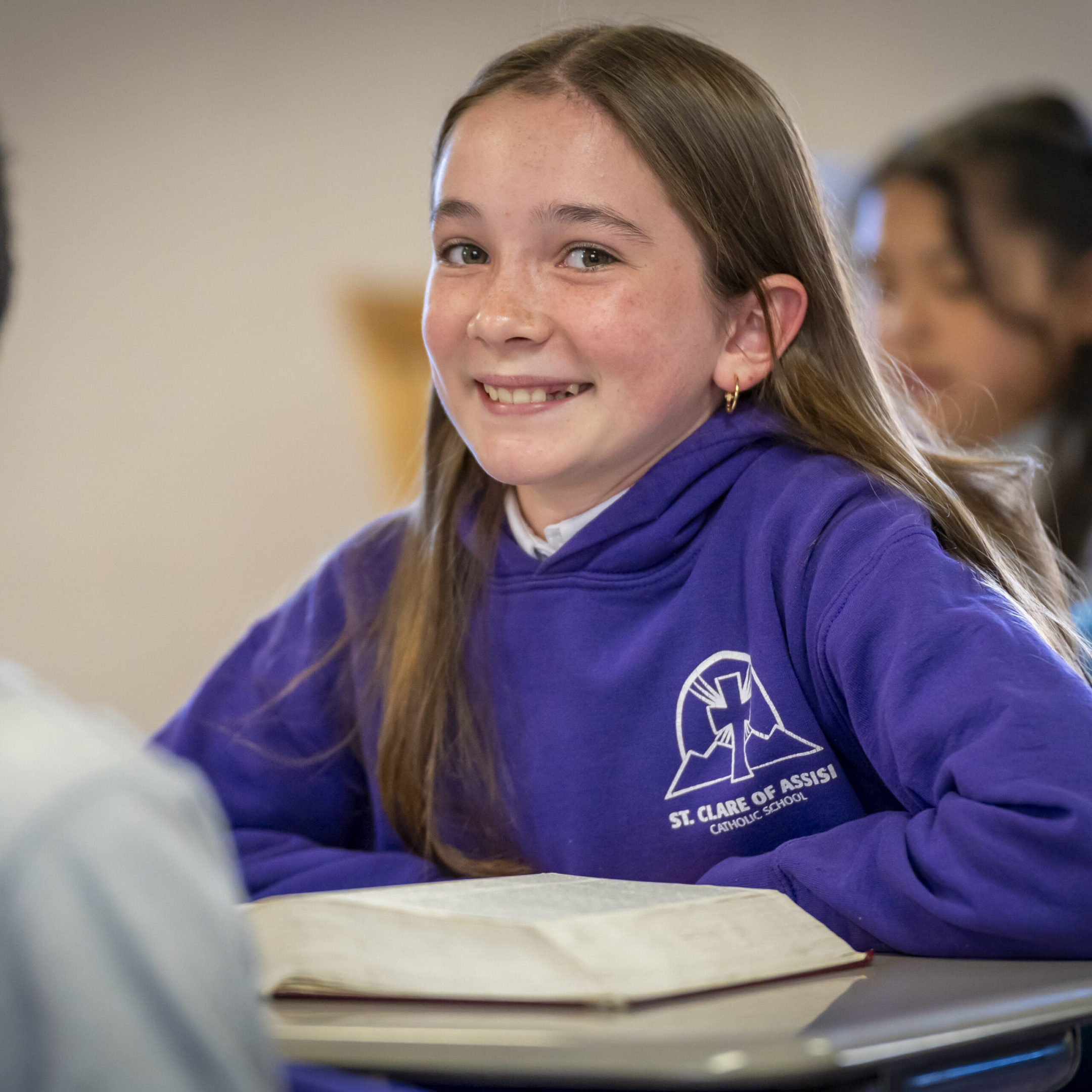 Smiling girl in purple school uniform sitting at desk.