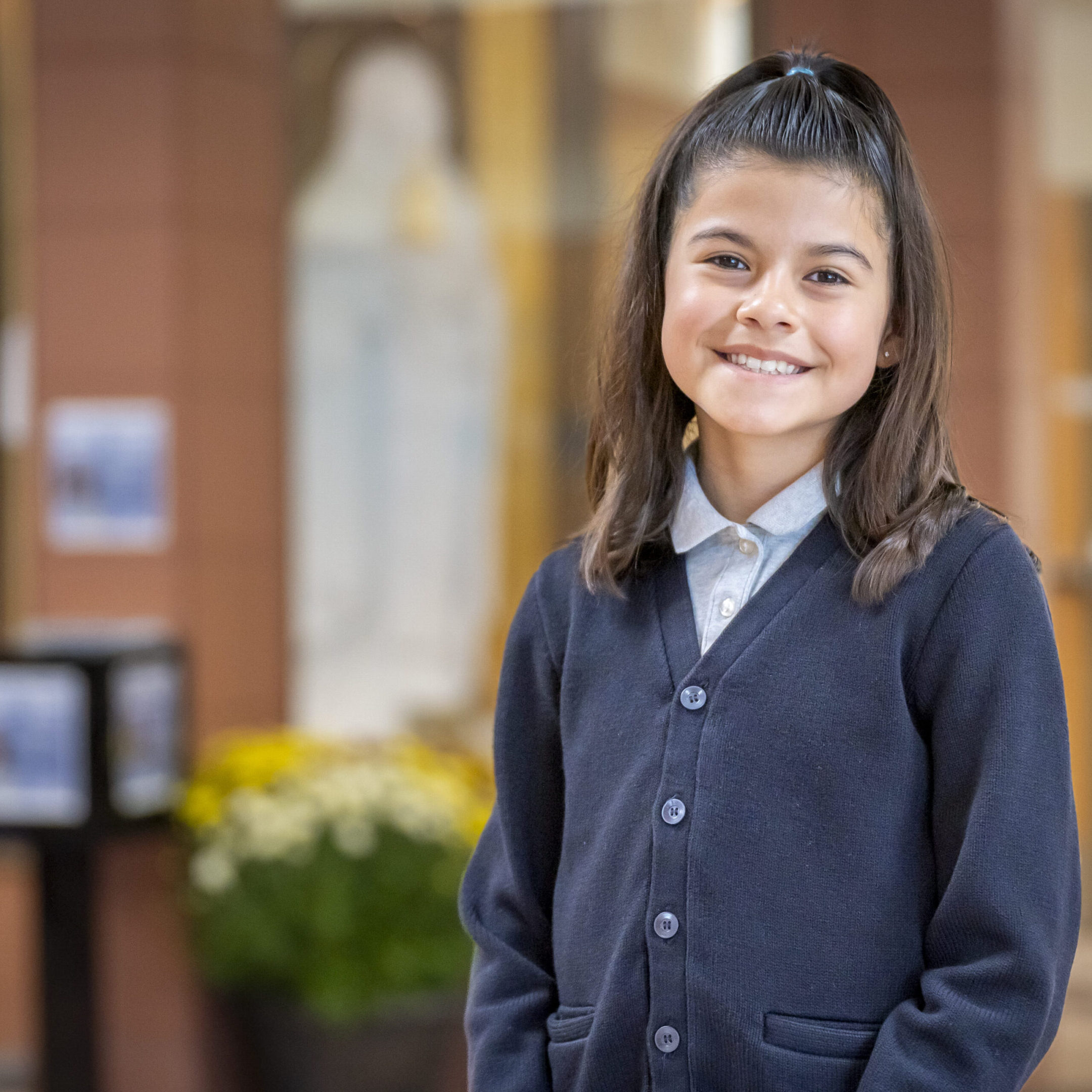 Smiling young girl in a school uniform standing indoors.