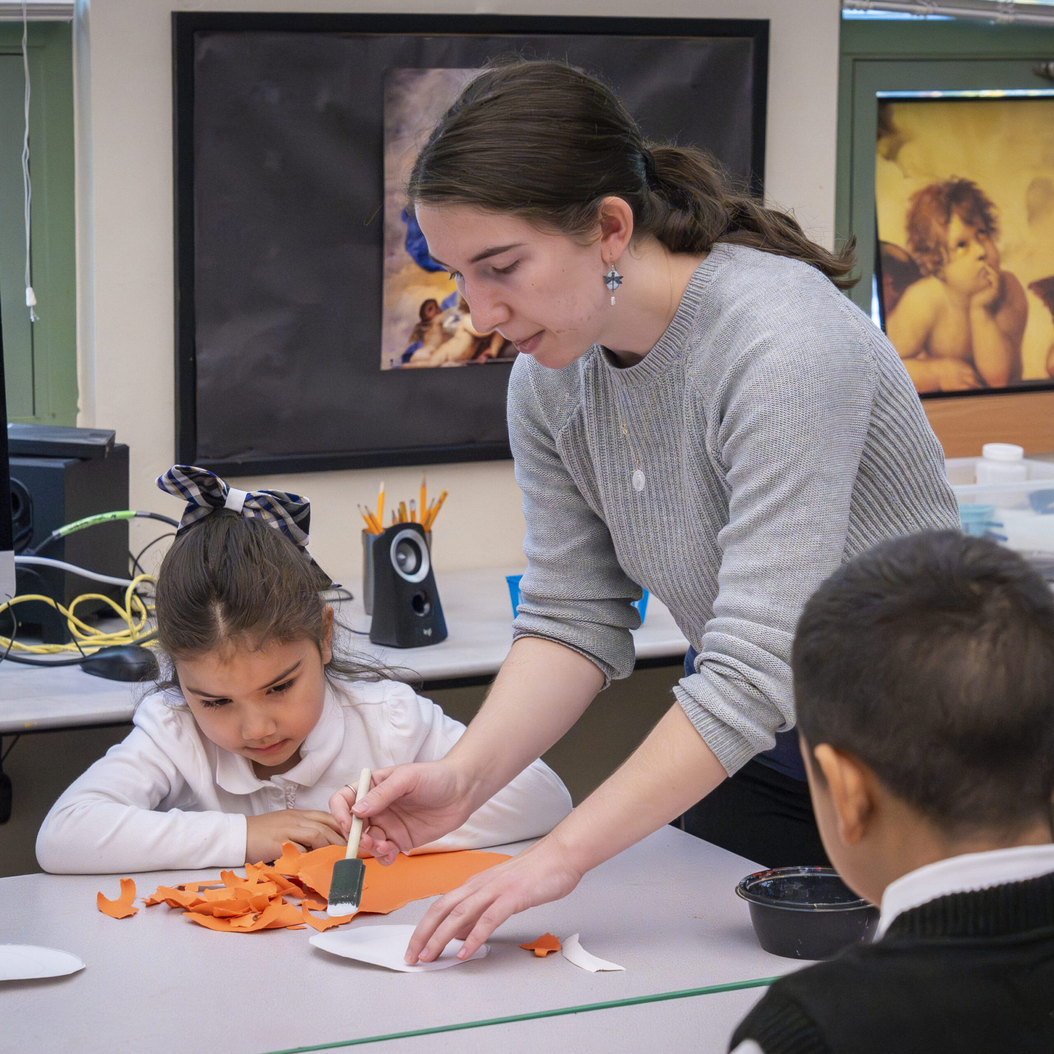 Teacher assisting young students with an activity at a classroom table.