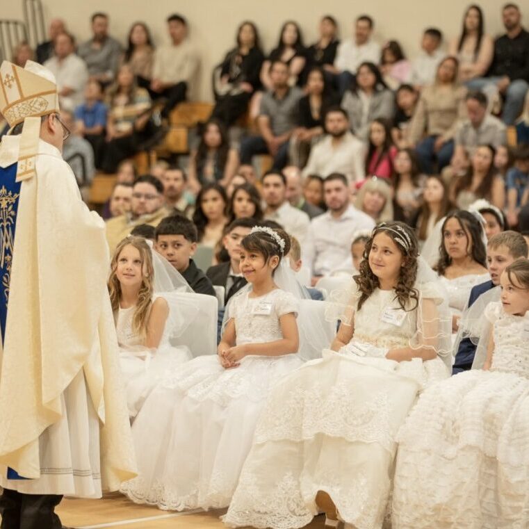 Girls dressed in white dresses attending a religious ceremony with a priest.
