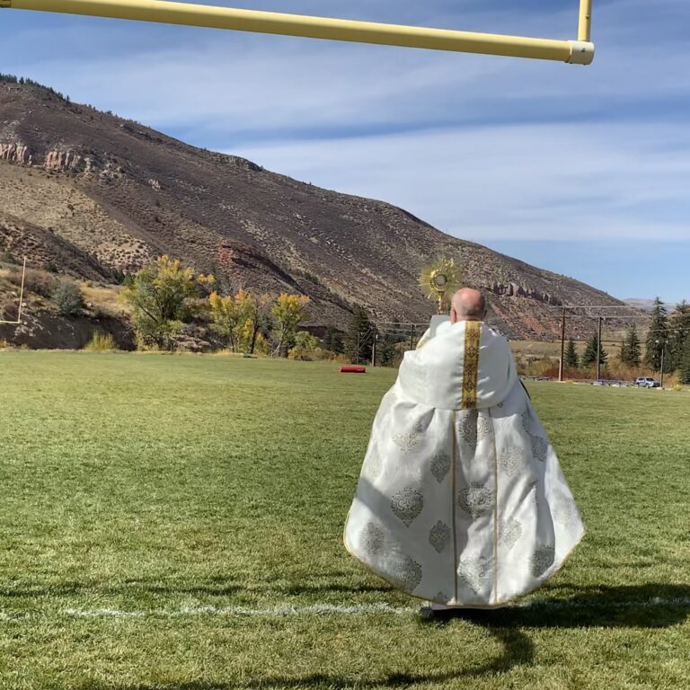 Person in a white robe walking on a football field under a goalpost.